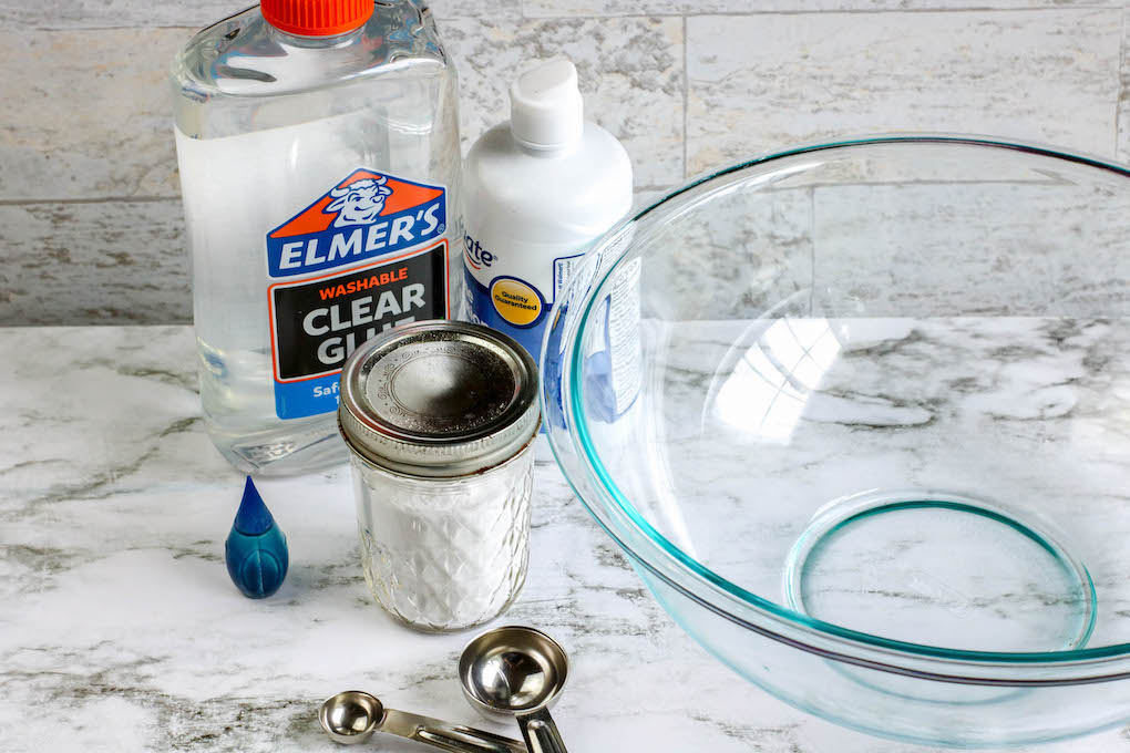 ingredients needed when making ocean slime with your kids include Elmers clear glue, baking soda, contact lens solutions, blue dye, silver glitter, and warm water.