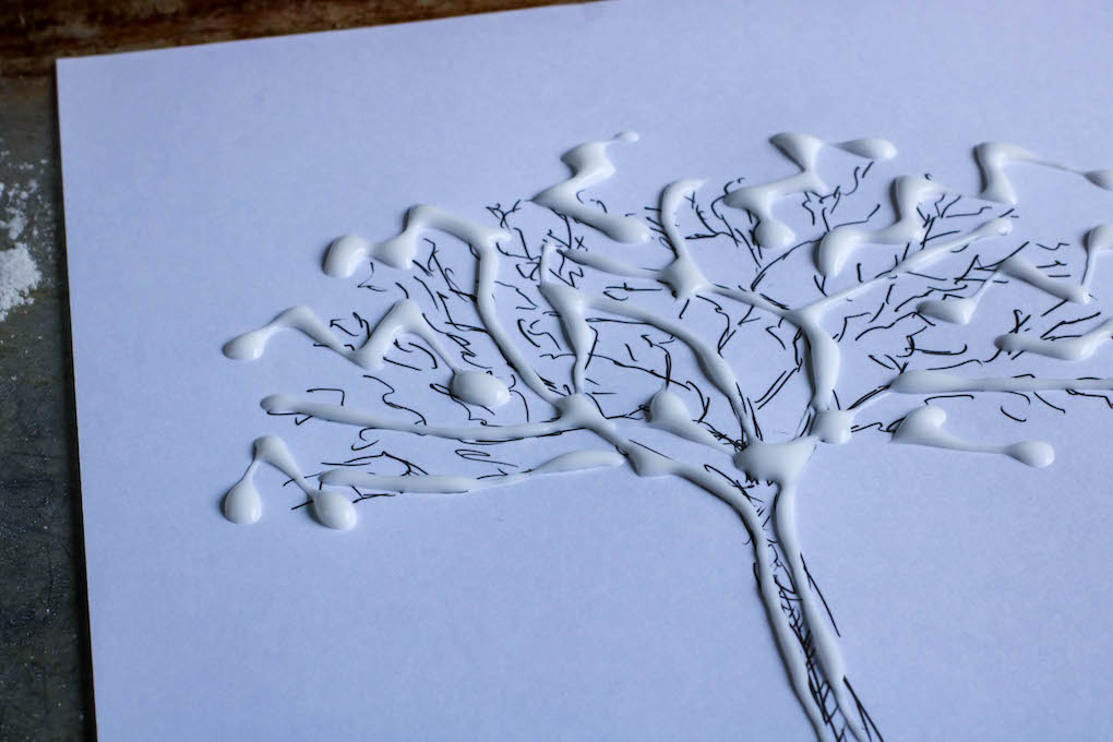 A line art tree template with blobs of glue applied on the branches on a white paper