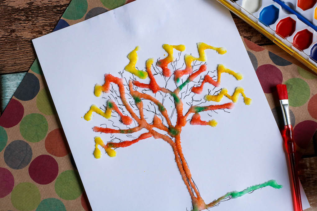 Salt and watercolor painting of a vibrant orange and yellow tree on a white paper