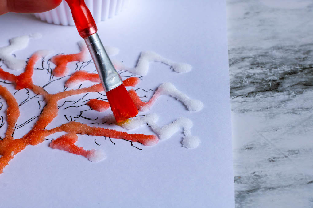 Hand painting orange watercolor over salt-glued tree template on paper