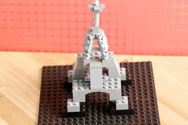 A small LEGO structure resembling the Eiffel Tower on a brown baseplate with a red grid background