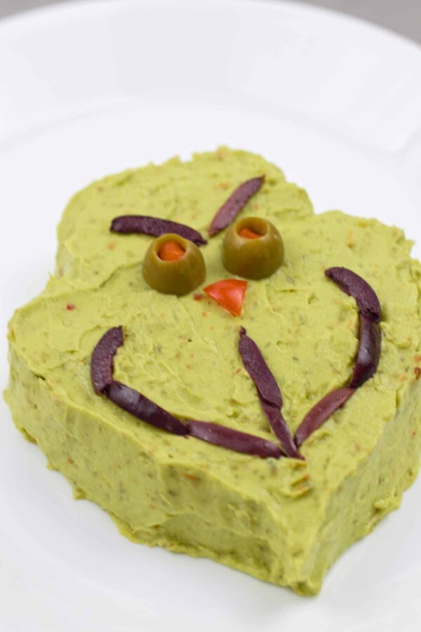 Grinch guacamole decorated with olive eyes and a tomato nose.