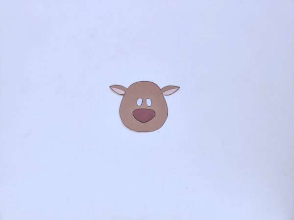 brown paper cut out of a reindeer's face with large unfinished white eyes a red nose and small ears