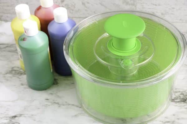 Green salad spinner and four bottles of colored liquid on a marble surface