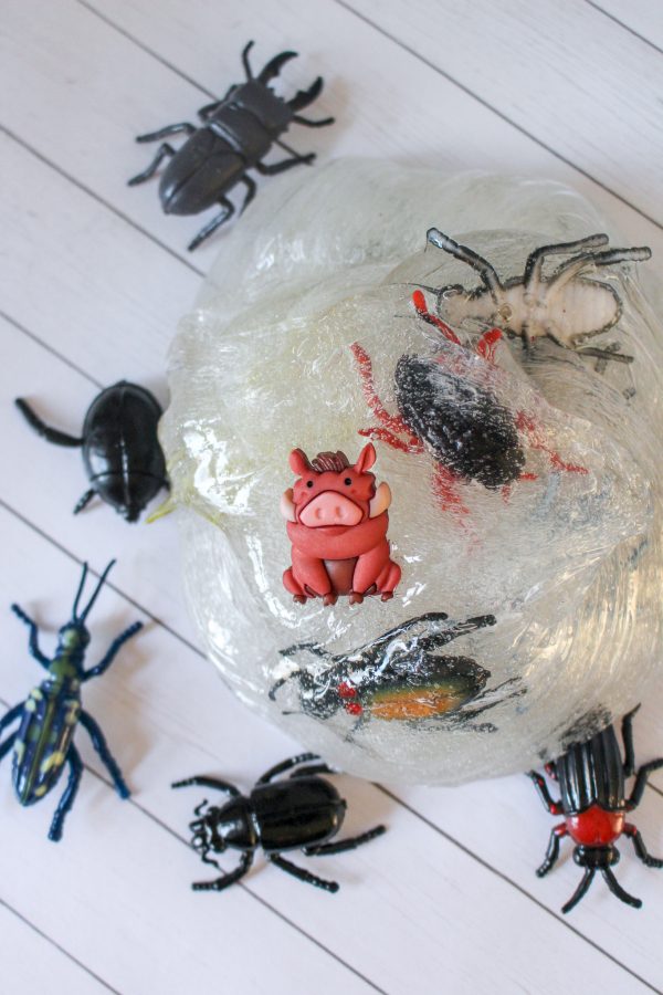 Toy pig and bugs on clear slime over a white wooden background ines on a textured white surface resembling bug slime recipe for kids homemade slime
