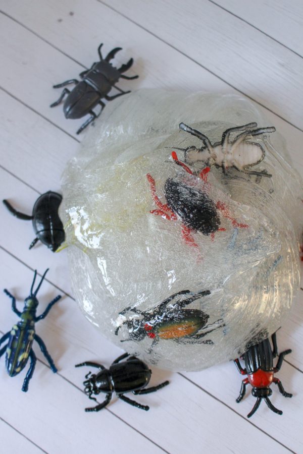 Clear slime with toy bugs on and around it, placed on a white wooden surface