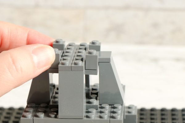 Hand assembling LEGO tower structure with grey bricks on black baseplate