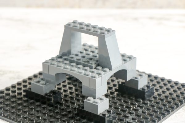 LEGO bridge structure on a black baseplate, with arch and supports