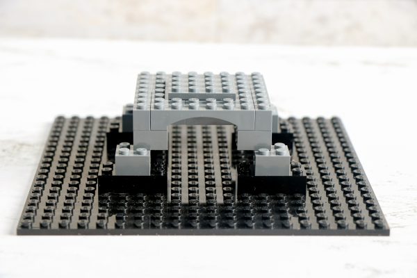 grey LEGO arch structure placed on a larger black LEGO baseplate, creating a bridge-like appearance