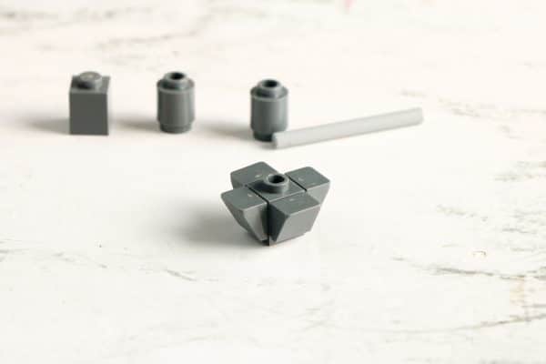 Gray LEGO bricks assembled into a cubic shape, with bricks and a long axle nearby on a white surface