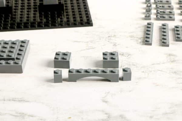 A grey LEGO structure with a bridged design, a black LEGO baseplate, and other grey LEGO pieces