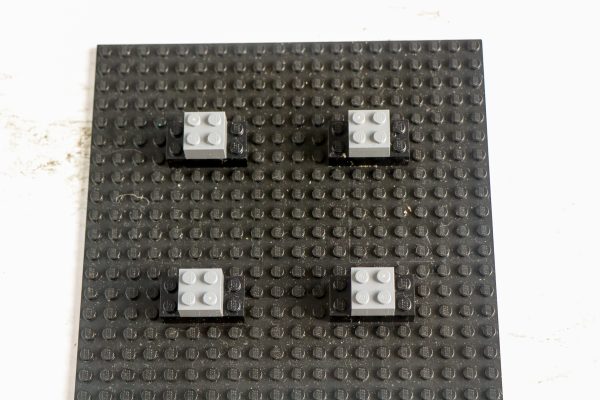 Four white LEGO bricks mounted on black blocks, evenly spaced on a black baseplate 