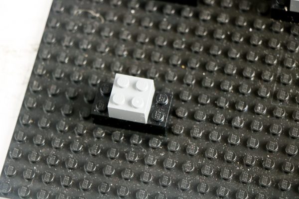 A single white LEGO brick placed on top of a black baseplate