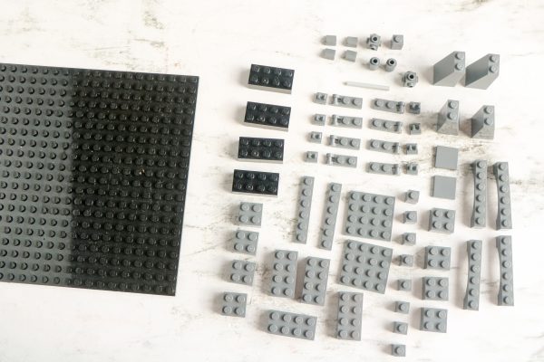 An assortment of grey LEGO bricks organized neatly beside a large black baseplate