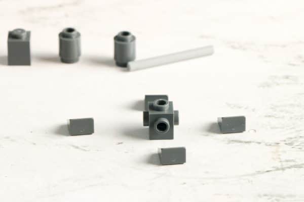 Assorted gray LEGO pieces including bricks, cylinders, and a long axle on a white surface