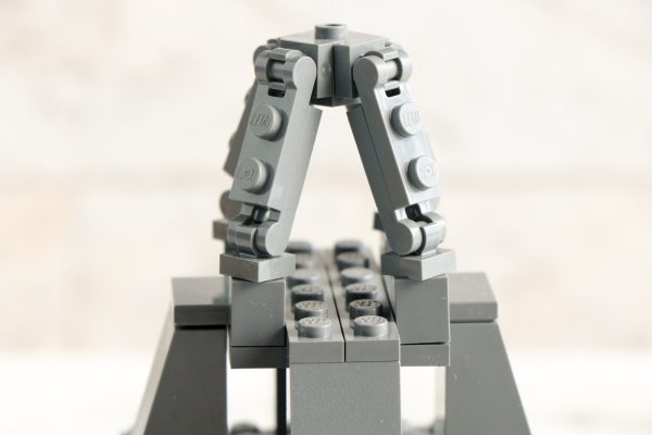 Close-up of a LEGO structure with arched grey pieces and LEGO logo, set on a grey base