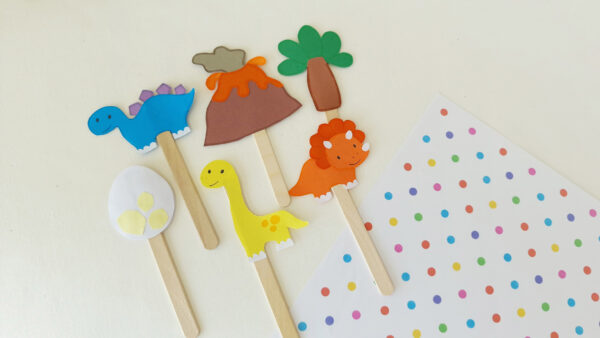 Dinosaur-themed popsicle stick puppets including a stegosaurus, volcano, tree, triceratops, dinosaur egg, and brachiosaurus.