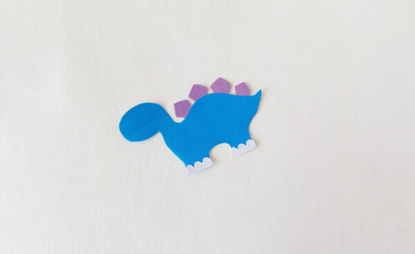 Partially assembled blue dinosaur with purple spikes and white feet for a popsicle stick puppet.