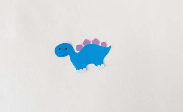 Completed blue dinosaur cut-out with purple spikes and drawn facial details for a popsicle stick puppet.