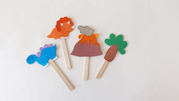 Dinosaur-themed popsicle stick puppets featuring a triceratops, stegosaurus, volcano, and tree.