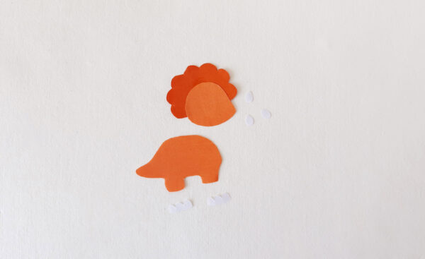 Cut-out pieces of an orange dinosaur for a popsicle stick puppet, including body, head, and details.