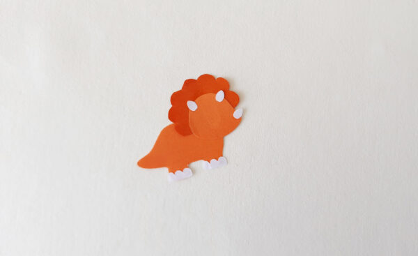 Fully assembled orange dinosaur cut-out for a popsicle stick puppet, with horns and feet attached.