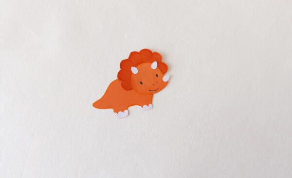 Completed orange dinosaur cut-out for a popsicle stick puppet, with drawn facial details.