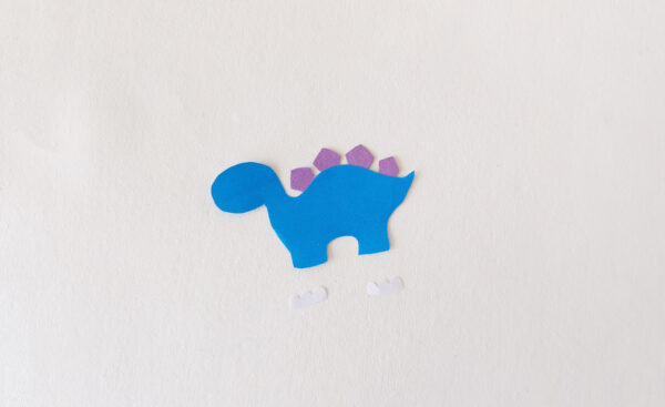 Cut-out pieces of a blue dinosaur with purple spikes for a popsicle stick puppet.