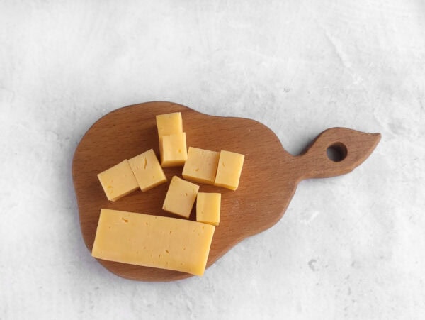 Cubed cheddar cheese on a small wooden serving board.