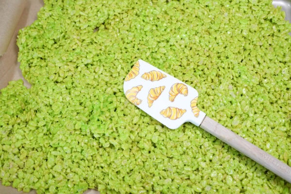 Green rice crispy mixture spread out on a surface with a spatula