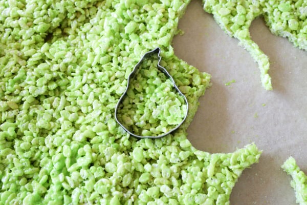Green rice crispy mixture being cut with a Grinch-shaped cookie cutter
