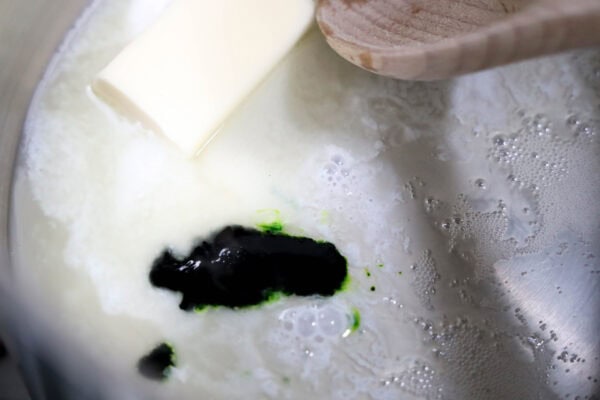 Close-up of melting butter and green food coloring being mixed in a pan with a wooden spoon