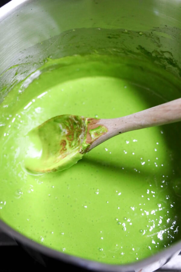 Pot of bright green melted mixture being stirred with a wooden spoon