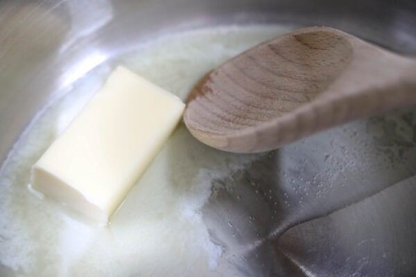 Close-up of a stick of butter melting in a pan with a wooden spoon stirring
