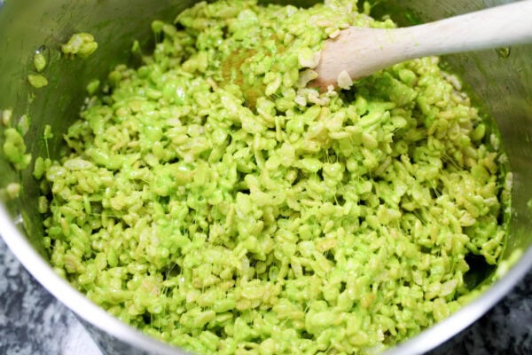Pot of green rice crispy mixture being stirred with a wooden spoon