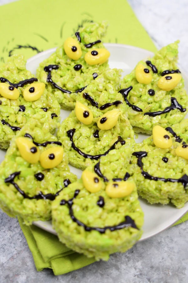 Plate of Grinch-themed green rice crispy treats decorated with yellow eyes and black icing to create Grinch faces