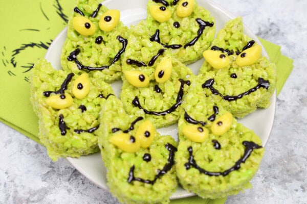 Plate of decorated Grinch-themed rice crispy treats with yellow candy eyes and black icing for faces
