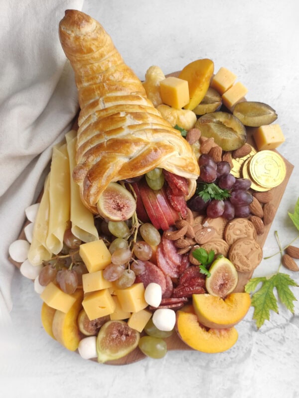 Close-up of puff pastry cornucopia overflowing with cheese, fruit, meats, and cookies.