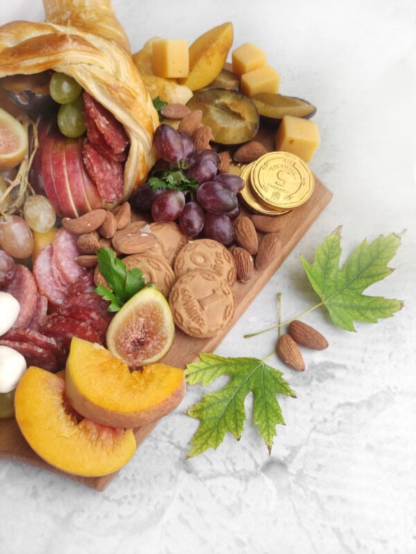 Close-up of fruit, cheese, cookies, almonds, and chocolate coins on the charcuterie board.