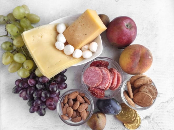 Charcuterie board ingredients with cheese, grapes, salami, fruit, almonds, and cookies.