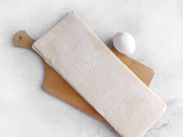 Thawed puff pastry and egg on a wooden cutting board.