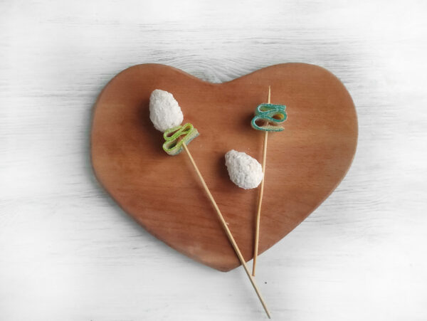 To create the white tulip, fold the green ribbon into an accordion and slide it onto the skewer. Next, unwrap a coconut candy and place it on the skewer.