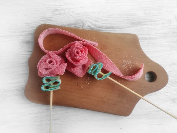 For the red rose, start by pinching the accordion-folded green ribbon in place. Begin wrapping the red ribbon to form a roll, making two or three turns. Twist the ribbon around its axis and keep wrapping until you reach the end of the ribbon. Secure the end with a skewer.