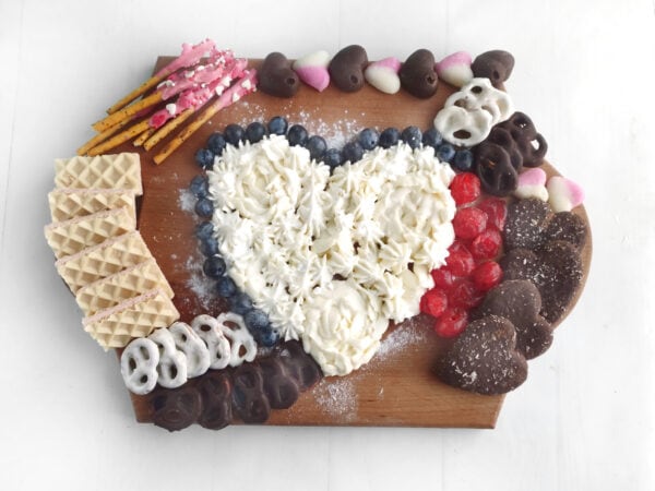 Arrange heart-shaped marshmallows, raspberries, and fresh fruit around the board to add vibrant color.
