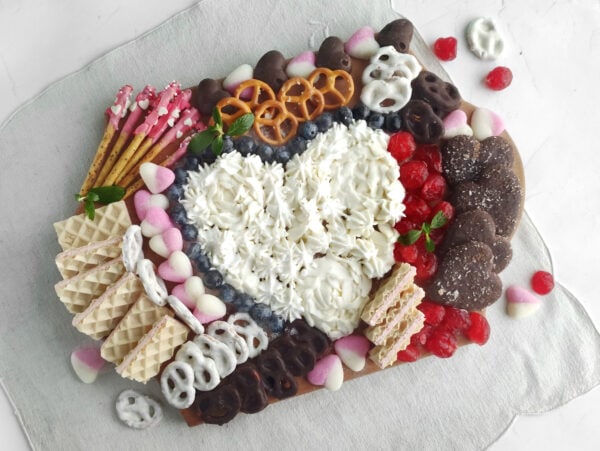 A colorful assortment of desserts arranged beautifully on a Valentine's-themed charcuterie board featuring candies and pastries.