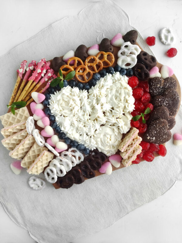 A festive charcuterie board filled with an array of Valentine’s Day desserts, including chocolates, cookies, and marshmallows.