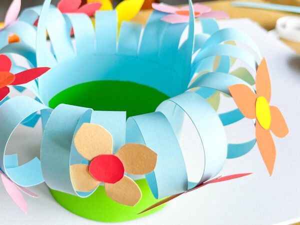 Fully decorated basket with a handle, adorned with multiple colorful paper flowers around the curled edges