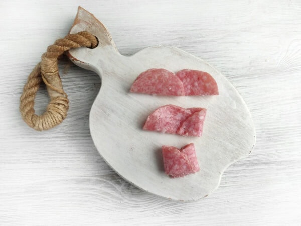 A small wooden cutting board with a rope handle, holding three pieces of sliced salami