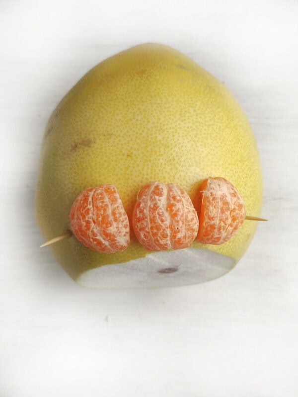 A pomelo topped with three tangerine slices skewered on toothpicks