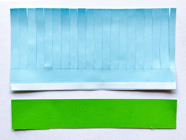 Blue and green paper are layered, with tape visible on the blue paper's bottom edge